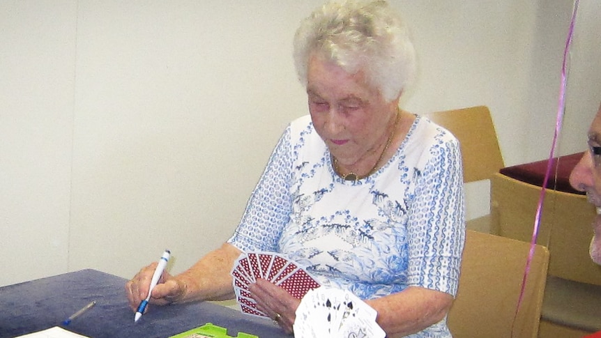 An elderly woman looking intensely at a hand of cards with a pen 