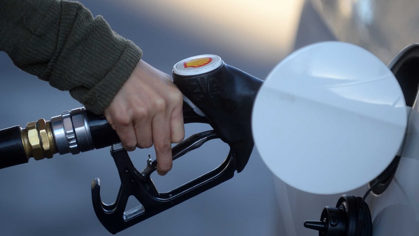 A hand holding a nozzle putting fuel in a white car