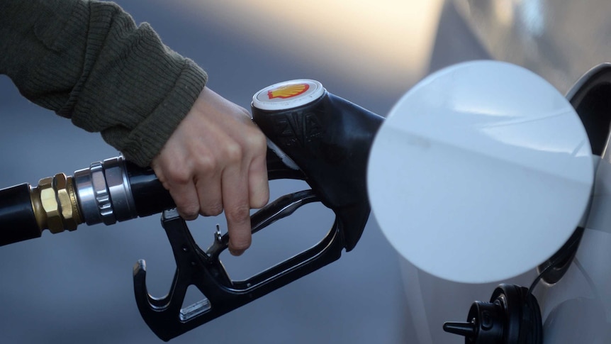 A hand holding a fuel nozzle putting petrol in a white car