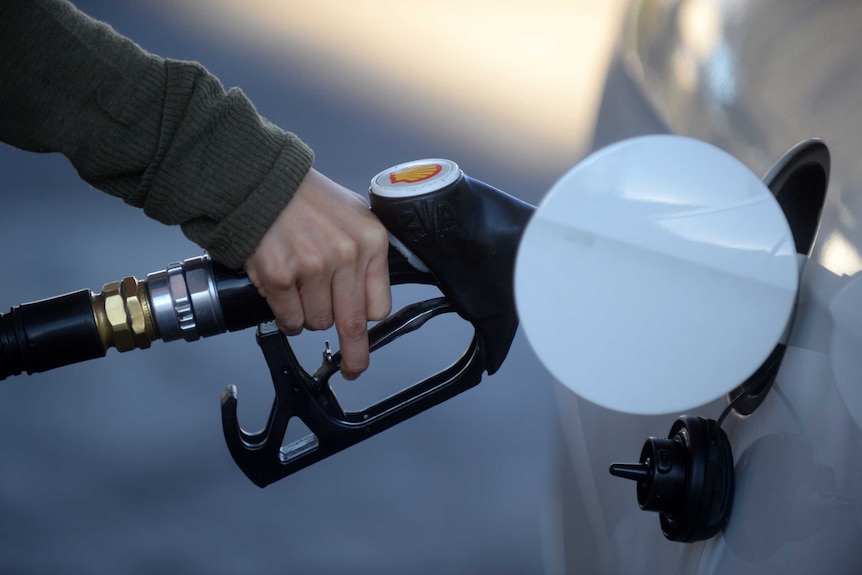 A hand holding a fuel nozzle putting petrol in a white car