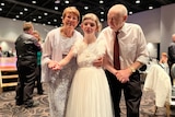 Young debutante with disabilities stands in the centre with a parent on each side, smiling and holding hands.