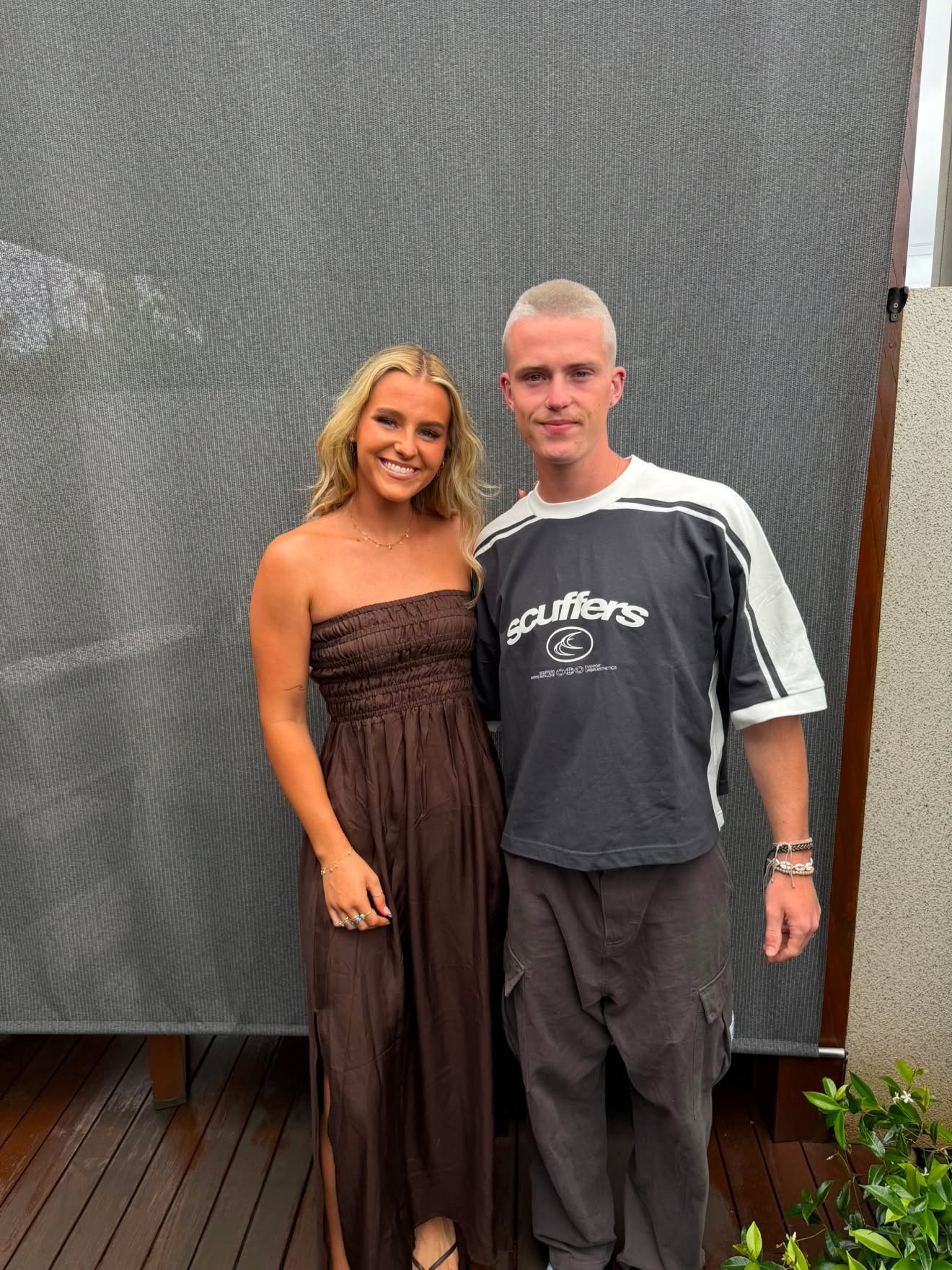 A smiling young blonde woman and a young man with cropped, light hair stand in a yard.