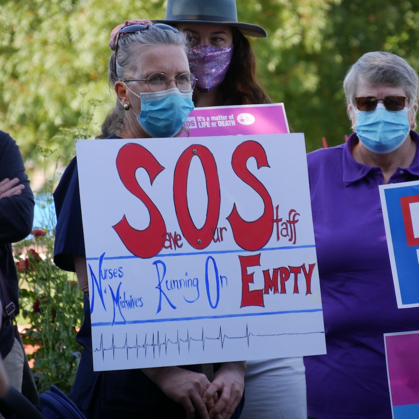 A nurse holds a protest sign that reads "SOS, nurses and midwives running on empty"