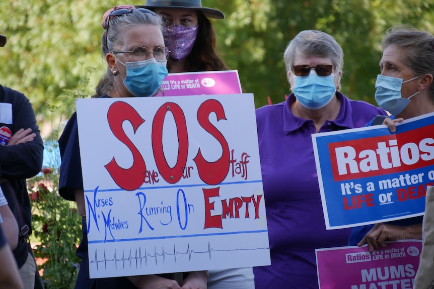 A nurse holds a protest sign that reads "SOS, nurses and midwives running on empty"