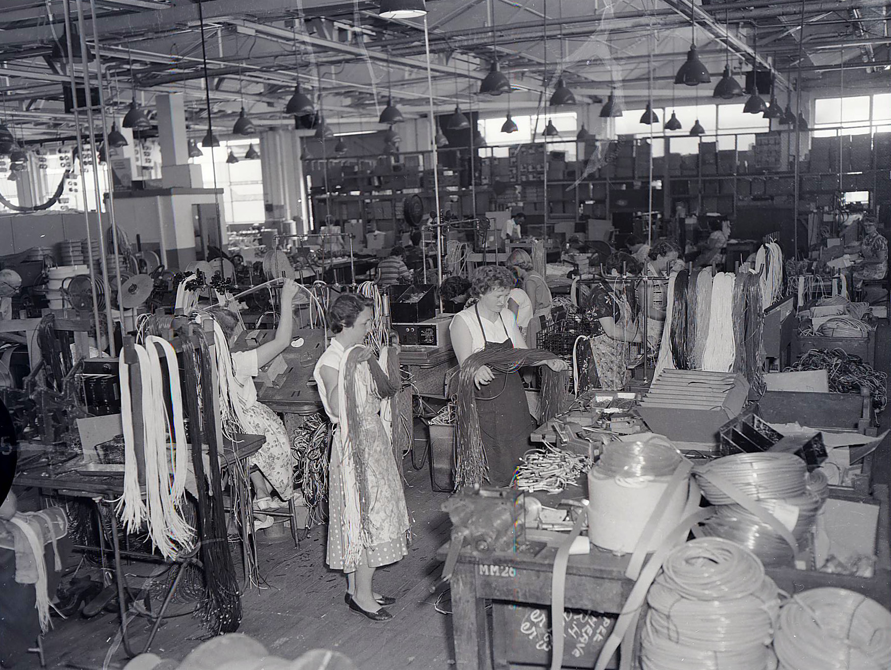A black and white photograph of women holding long cords over their arms in a factory