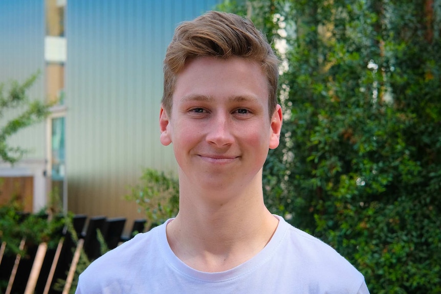 A young man with blonde hair and blue t-shirt smiles at the camera