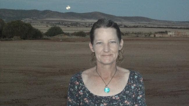 A middle-aged woman with paddocks, hills and the moon in the background.