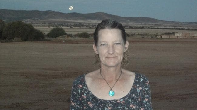 Tamara Ann Turner stands in a paddock, with hills and the moon in the background.
