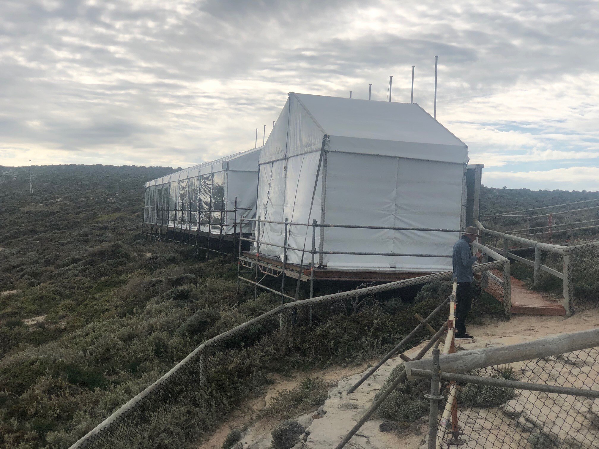 A large white tent structure on sand dunes with native shrubs around.