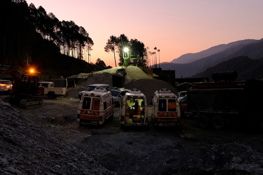 Three ambulances are parked under flood lights outside a tunnel where workers are trapped.