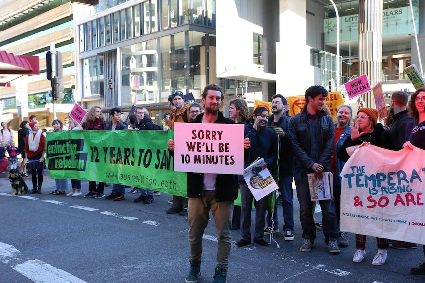 Activist holds sign saying 'sorry we will be 10 minutes' as they block traffic in city.