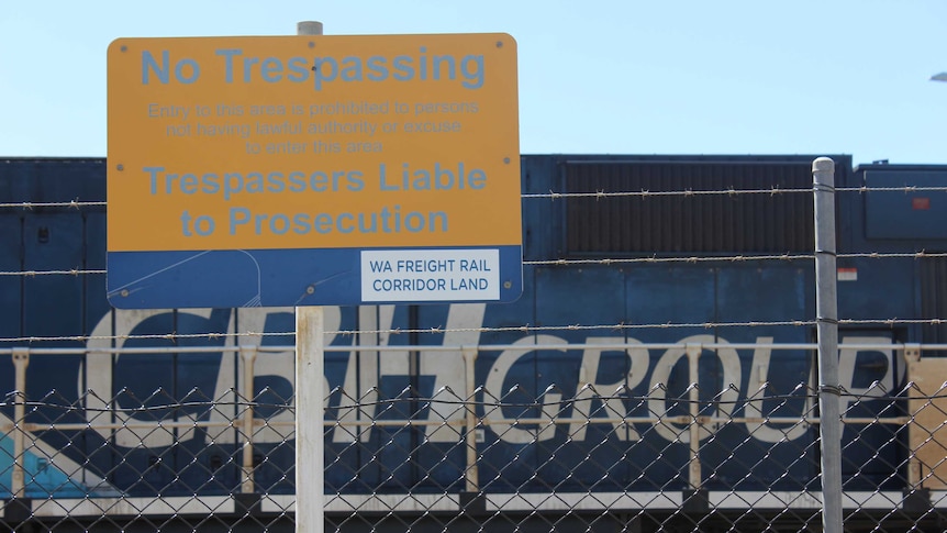 A trespass sign in front of a blue railway locomotive.