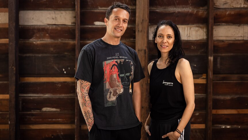Moss Te Ururangi Patterson (left) and Deborah Brown (right) stand side by side in front of a wooden wall smiling at the camera.