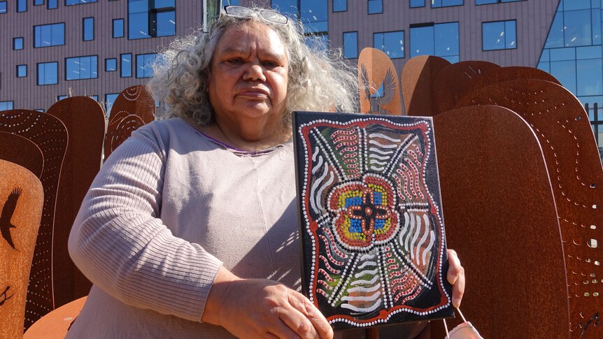 An Indigenous woman shows a painting she has done.