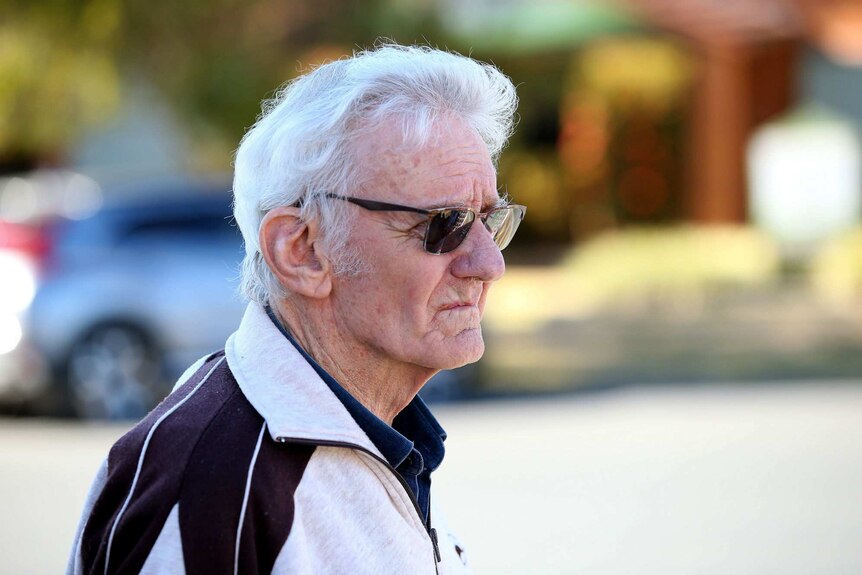 A man with white hair wearing a tracksuit jacket.
