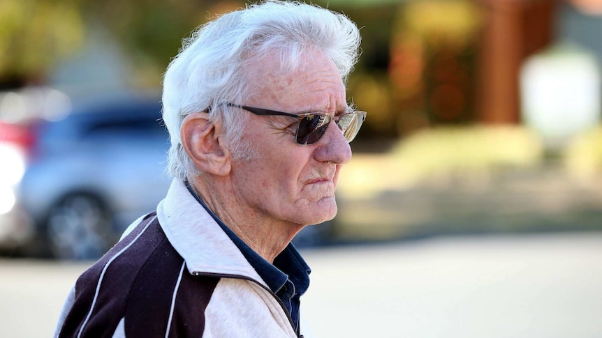 A man with white hair wearing a tracksuit jacket.