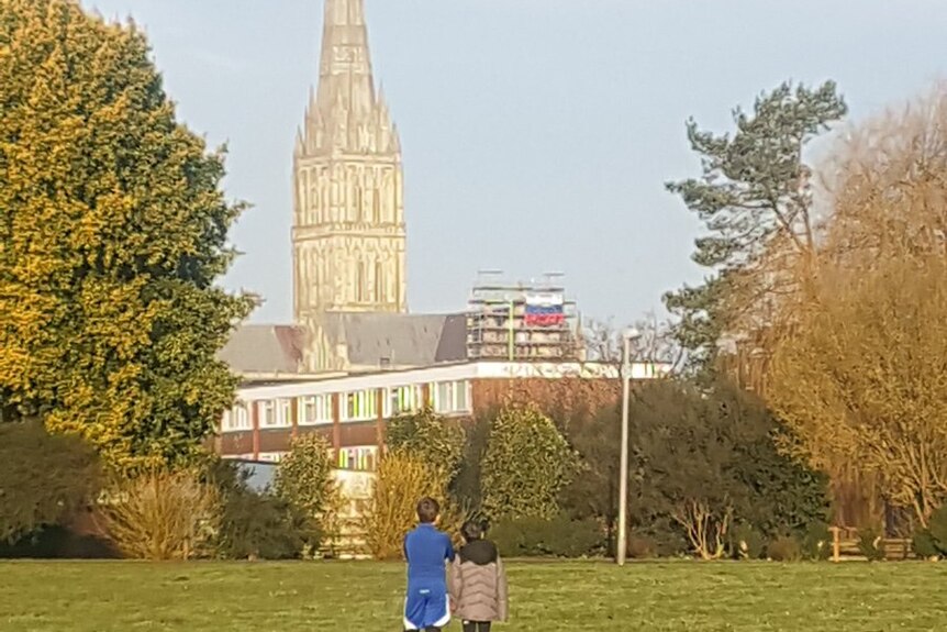 Russian flag hangs off the scaffolding on the Salisbury Cathedral while two children look at it from a park.