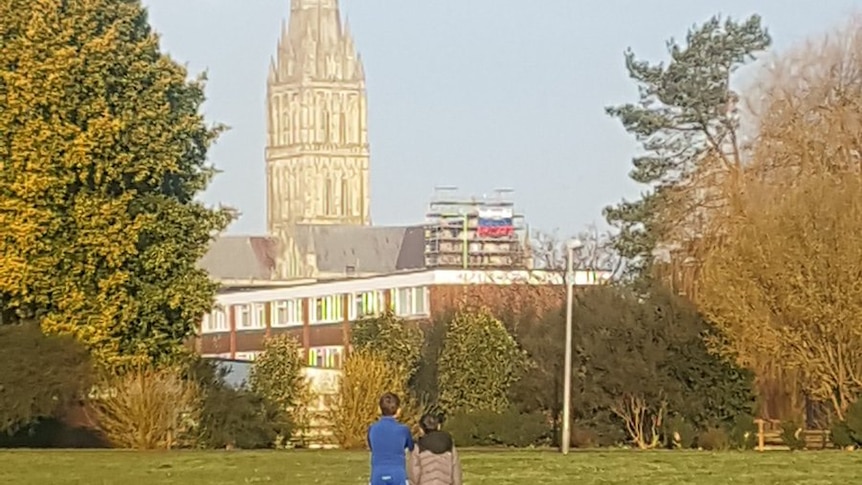 Russian flag hangs off the scaffolding on the Salisbury Cathedral while two children look at it from a park.