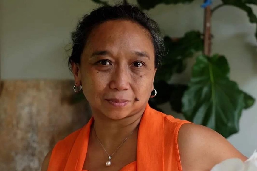 A woman looking at the camera, wearing orange traditional blouse.