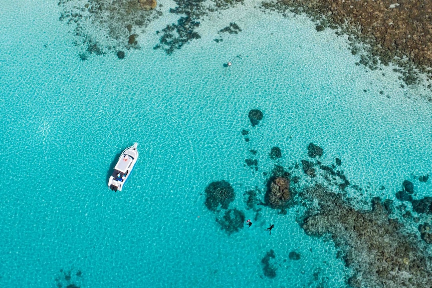 An aerial shot looking down at a white boat over turquoise waters and rocky corals 