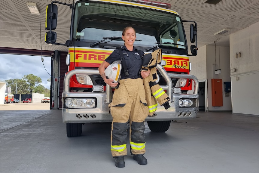 A woman stands in front of a fire truck. She is smiling.