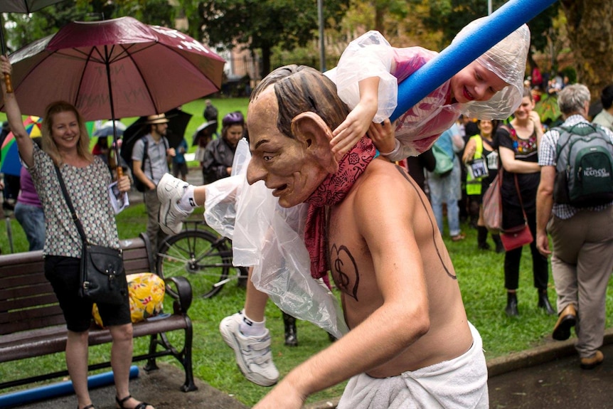 A protester dressed as Tony Abbott carries a child through the crowd at the Sydney March in March.