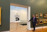 A black and white ink drawing stands on an easel in an art gallery.