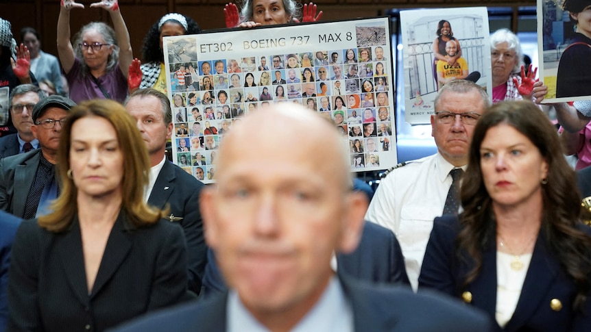 A mans face close up and a women holds a poster with the faces of all those killed in a place crash 