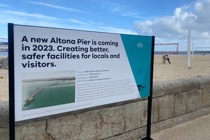 A sign detailing the new Altona Pier redevelopment is pictured with locals playing volleyball on the beach in the background