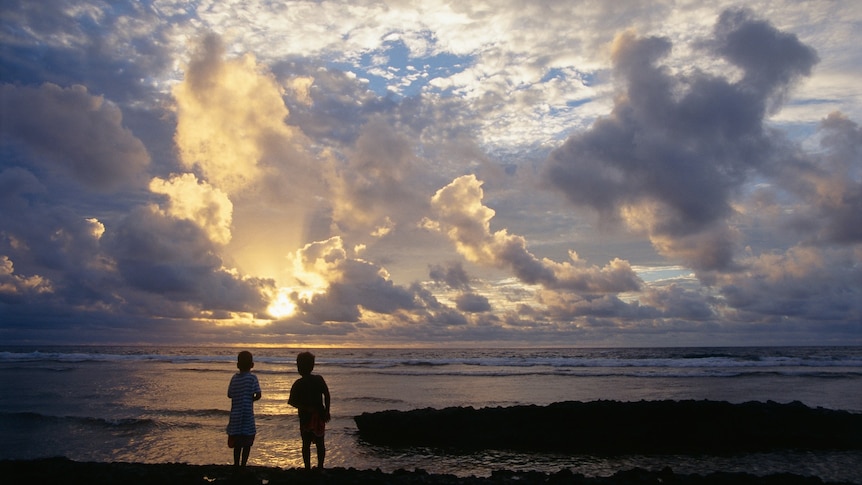 Two boys silhouetted against a sunrise over the ocean.