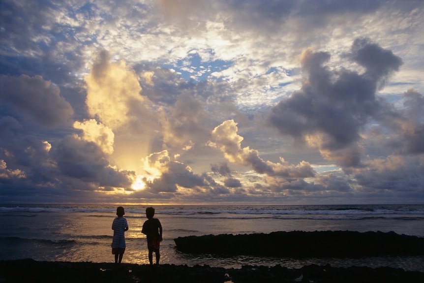 Two boys silhouetted against a sunrise over the ocean