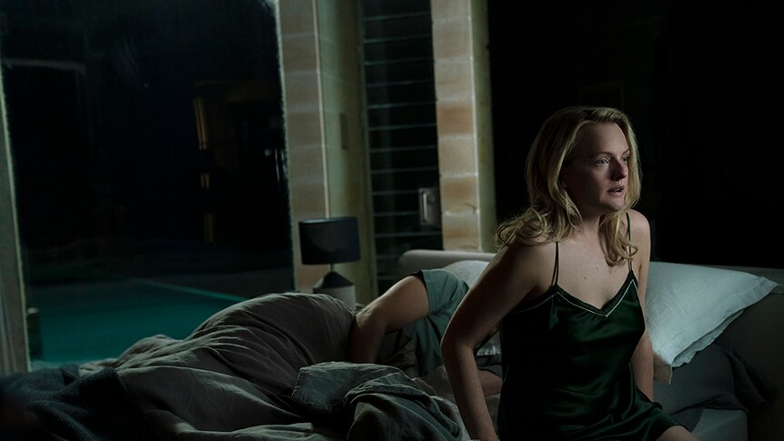 A woman with blonde hair and scared expression sits up in bed in the middle of the night, behind her a man lies asleep.