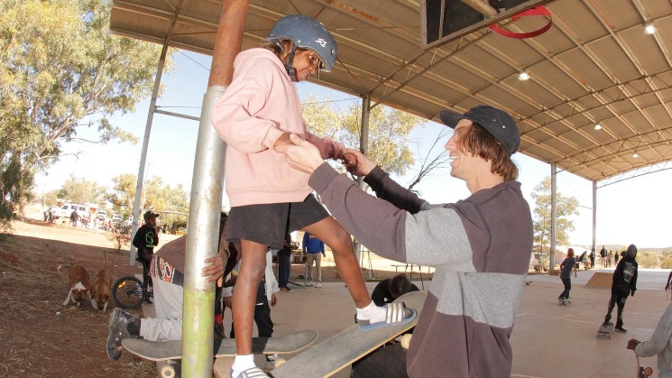 A man helps a young boy stand steady on a skateboard perched at the top of a quarterpipe.