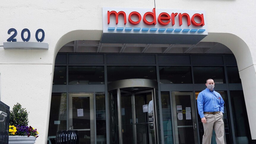 A man in a face mask walks outside the glass doors of Moderna Inc's offices, with Moderna's logo mounted above