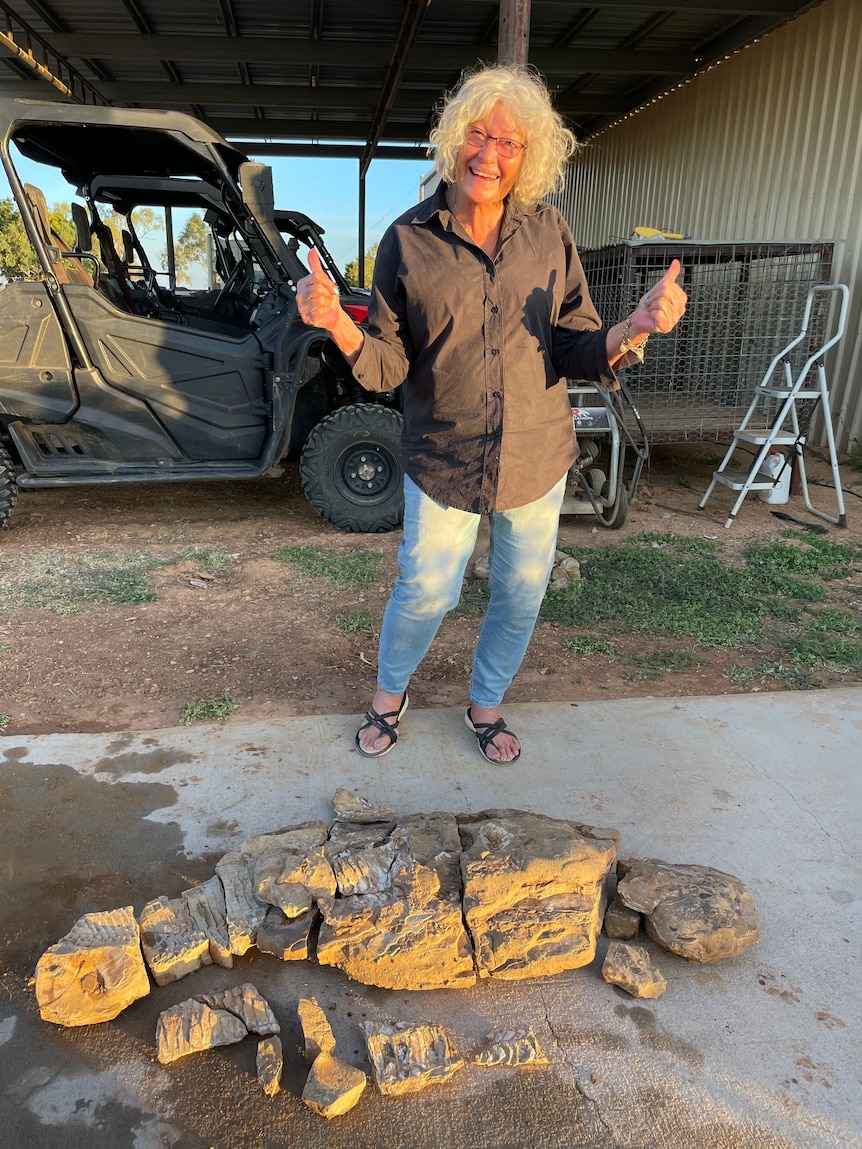 Woman stand holding up thumbs next to fossils