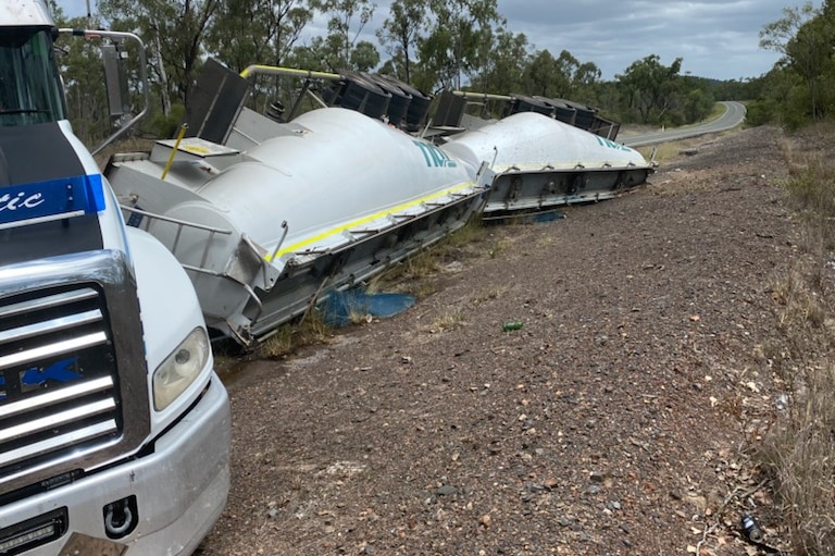 B-double truck trailers have rolled onto their side along a rural road