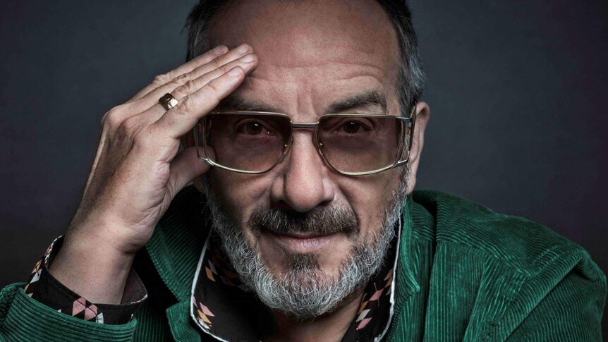 Close up of Elvis Costello with grey beard wearing gold rimmed sunglasses and a green corduroy jacket