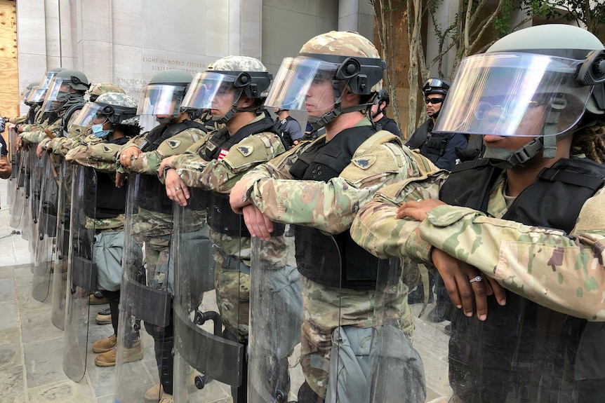 Line of heavily armed soldiers in riot gear.