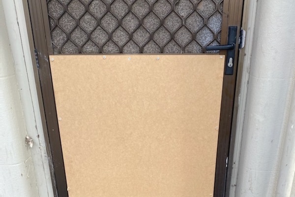 A brown board over a damaged screen door.