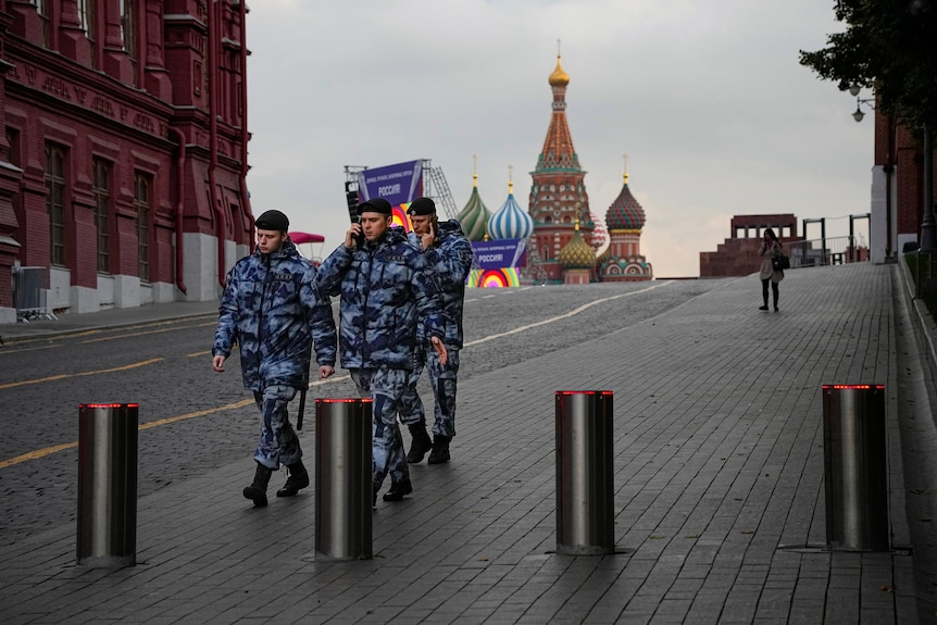 three soldiers walk on cobbled stones with the turrets of the catehdral just visible behind them