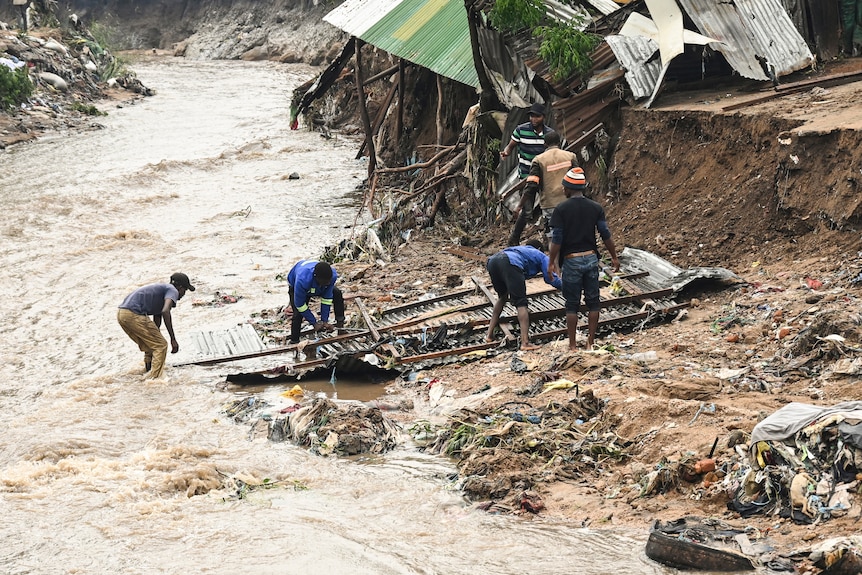Men salvage parts from their destroyed home as water and mud rushes past.
