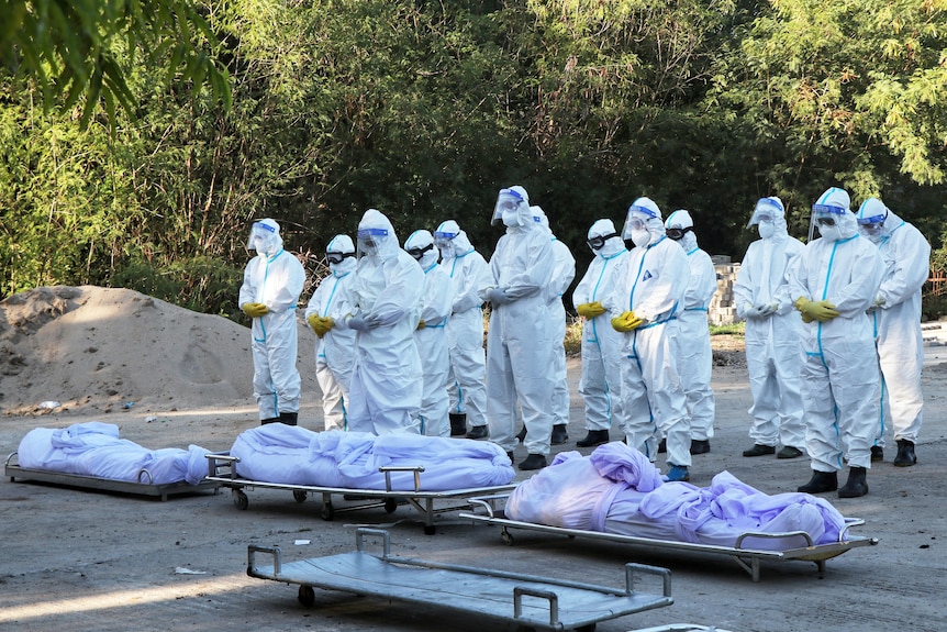 Volunteers in full PPE pray in front of the bodies of three people who died of COVID