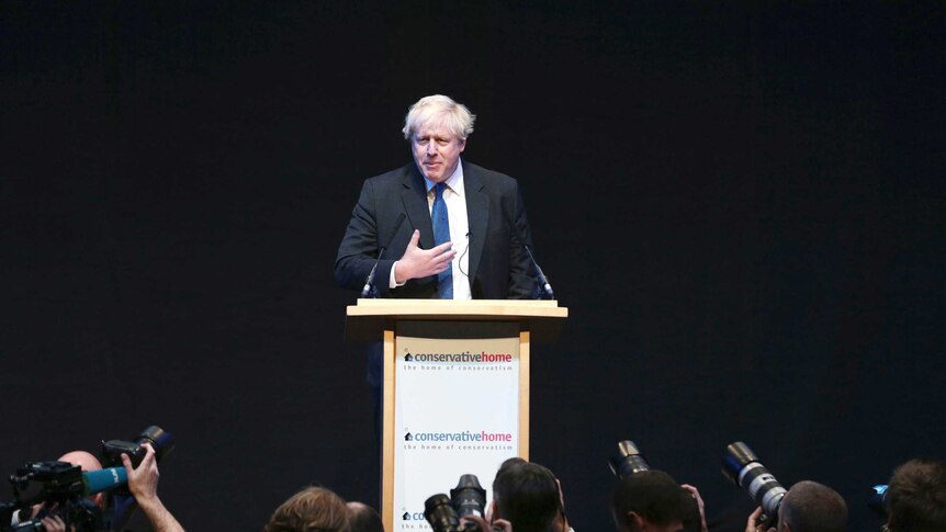 Boris Johnson stands behind a lectern while photographers take pictures