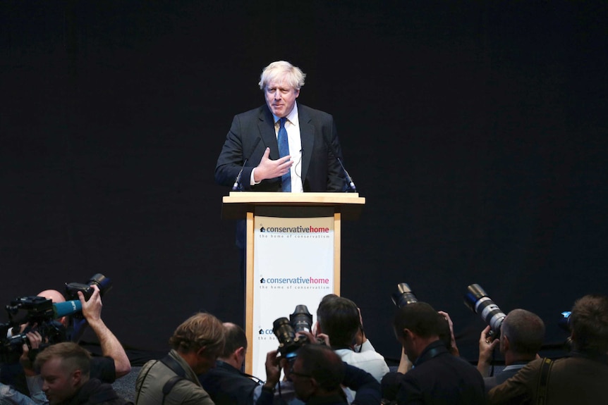 Boris Johnson stands behind a lectern while photographers take pictures