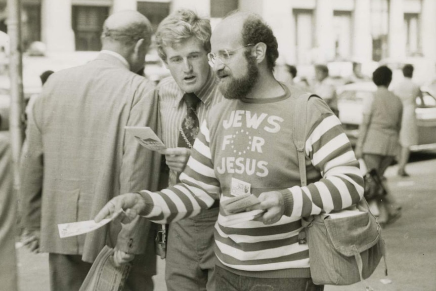 Black and white photo of David Stern handing out leaflets wearing Jews for Jesus t-shirt.