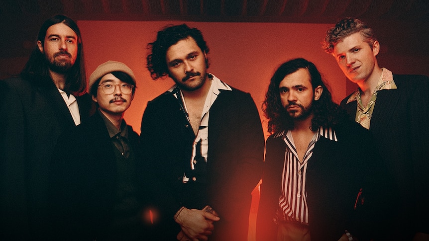 The band members of Gang Of Youths stand in front of a red background facing the camera.