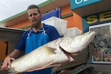 Commercial fisher Nathan Rynn from Townsville holding a large freshly caught barramundi next to his boat