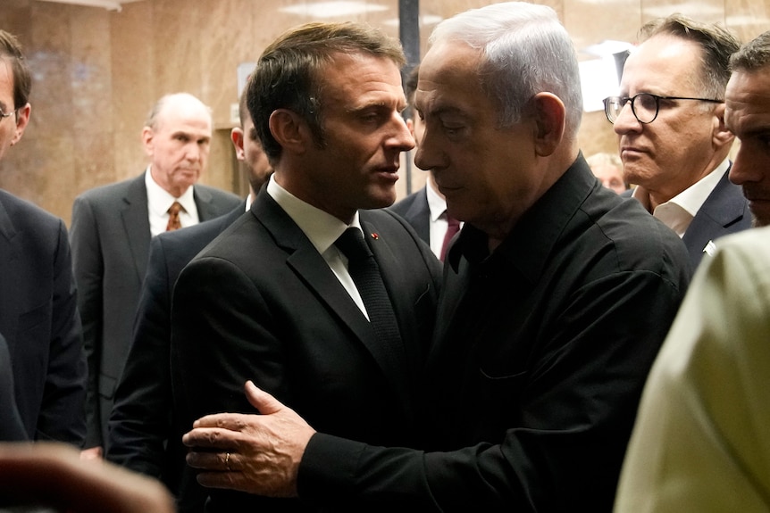 Emmanuel Macron and Benjamin Netanyahu lean in close to each other for a handshake and embrace
