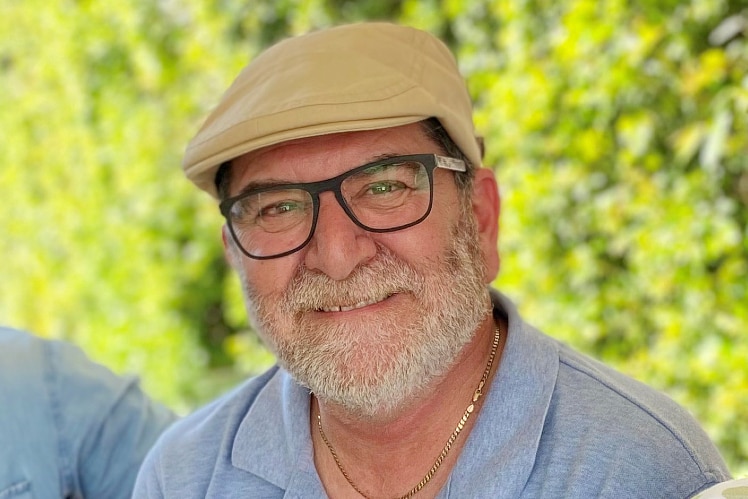 Man with a gentleman's cap on and glasses, gently smiling