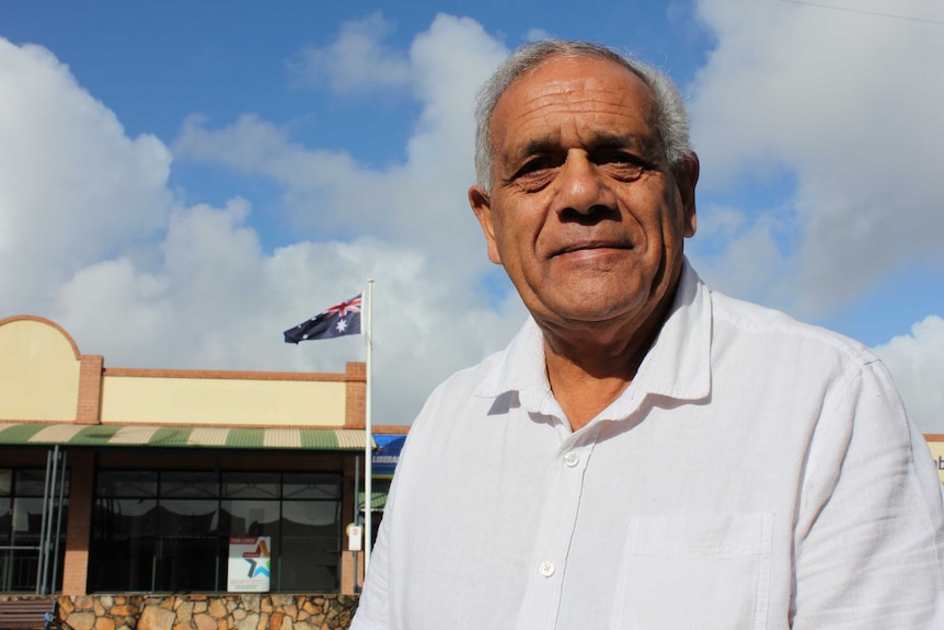 An Indigenous man standing in front of an Australian flag on a flagpole